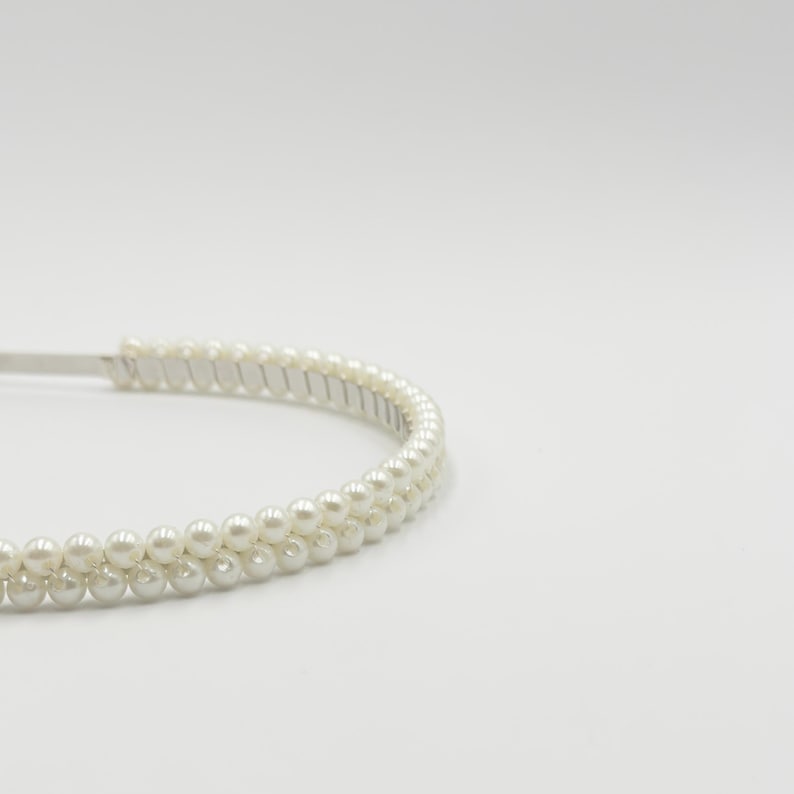 May include: A white headband adorned with two rows of faux pearls. The hair accessory features a silver-toned band. The small, evenly spaced pearls give a delicate and elegant appearance. The headband is designed for hair styling.