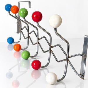 Peut inclure: Un porte-manteau mural composé d'une structure en métal argenté au design en zigzag. Le support comprend plusieurs crochets, chacun surmonté d'une boule ronde et lisse de différentes couleurs, notamment bleu, orange, vert, rouge et blanc.