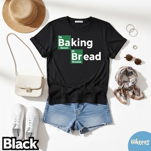 Puede incluir: Camiseta negra con las palabras "Baking Bread" en blanco, combinada con pantalones cortos de mezclilla, zapatillas blancas, un sombrero de paja, un bolso blanco y una bufanda estampada. El diseño de la camiseta incorpora elementos de la tabla periódica.