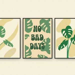 Puede incluir: Conjunto de tres láminas enmarcadas. Cada lámina presenta un diseño botánico con hojas y tallos verdes de monstera sobre un fondo crema y amarillo. La lámina central tiene las palabras "NO BAD DAYS" en verde.