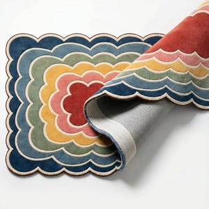 May include: A multi-coloured rug with a scalloped edge and a layered design. The rug features shades of blue, green, yellow, pink, and red. The rug is partially rolled, revealing its underside. The design is reminiscent of a flower or cloud.