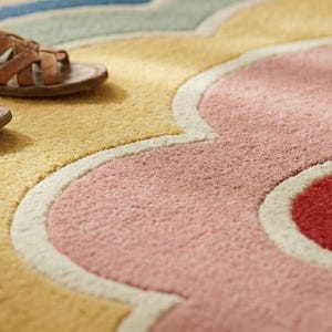 May include: A close-up shot of a patterned rug in yellow, pink, and red hues. Two brown leather sandals are placed on the rug, creating a relaxed, casual atmosphere. The rug has a floral design.