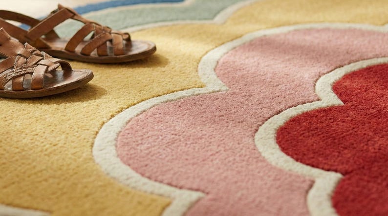 May include: A close-up shot of a patterned rug in yellow, pink, and red hues. Two brown leather sandals are placed on the rug, creating a relaxed, casual atmosphere. The rug has a floral design.