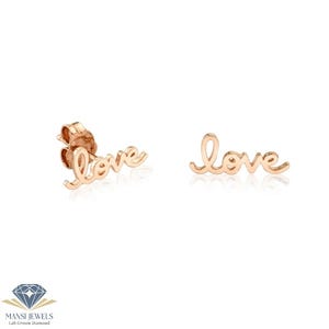 Puede incluir: Un par de pendientes de oro rosa con la palabra "love" escrita en cursiva. Los pendientes se muestran sobre un fondo blanco, resaltando su delicado diseño y acabado pulido.