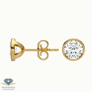 Op de afbeelding: Een paar gouden oorstekers met een ronde, heldere diamant in het midden. De oorbellen zijn gezet in een bezel-zetting en hebben een stift- en vlindersluiting. Gepresenteerd op een witte achtergrond.