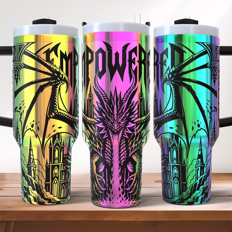May include: Three stainless steel tumblers with a gradient rainbow finish. Each tumbler features a black dragon and castle design with the words "EMPOWERED" in a gothic font. The tumblers have a white lid and a black handle.