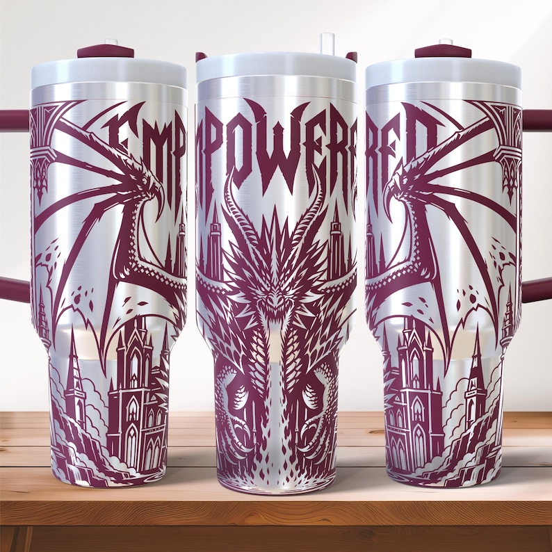 May include: A silver insulated tumbler with a dragon and castle design in burgundy. The word "EMPOWERED" is displayed in a gothic font. The tumbler has a white lid and a burgundy handle.