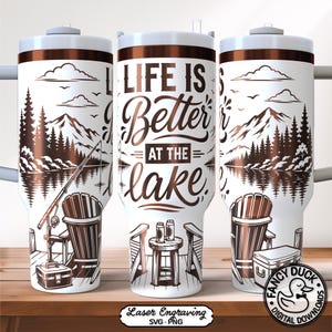 May include: White and brown insulated tumbler with a lake scene design. The design includes mountains, trees, a fishing rod, and the text "LIFE IS Better AT THE lake." The tumbler has a white lid and a brown band.