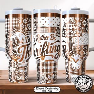 May include: Three stainless steel tumblers with white lids and copper-colored accents. Each tumbler features a unique design, including the text "I'd Rather Be Thrifting" and various decorative patterns and illustrations. The tumblers are on a wooden surface.