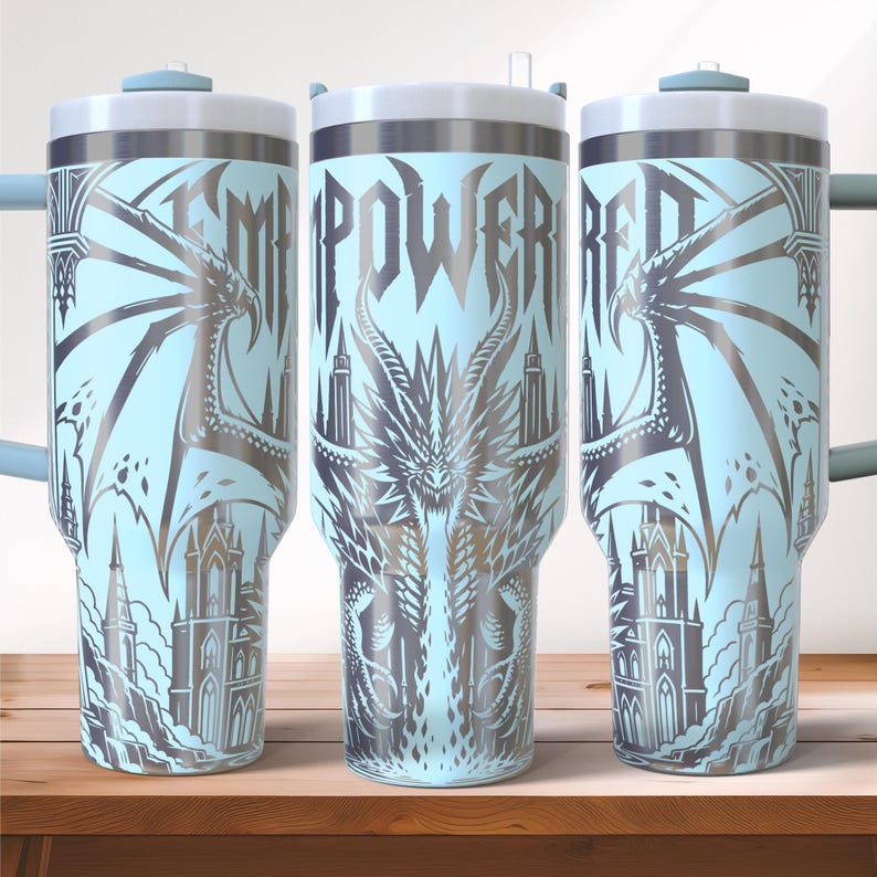 May include: A light blue tumbler with a silver dragon and castle design. The word "EMPOWERED" is displayed vertically. The tumbler has a silver rim, a white lid, and a handle.