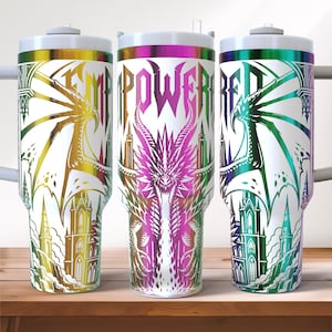 May include: Three white insulated tumblers with colorful dragon and castle designs. Each tumbler features the word "EMPOWERED" in a bold, stylized font. The dragons and castles are rendered in shades of gold, purple, and green.