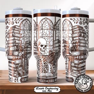 May include: A white and brown tumbler featuring a skeleton reading a book, surrounded by stacks of books. The design includes floral accents, a stained-glass window, and the text "SECRET READERS" and "SOCIETY OF FERAL READERS".