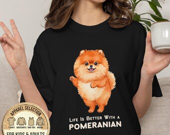 May include: A black short-sleeved t-shirt featuring a graphic of a fluffy orange Pomeranian dog. Below the dog, the text reads "LIFE IS BETTER WITH A POMERANIAN". A circular badge in the corner displays icons for t-shirts, sweatshirts, tank tops, and hoodies.