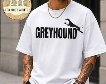 May include: A white short-sleeved t-shirt featuring the word GREYHOUND in bold black capital letters, accompanied by a black silhouette of a running greyhound dog. The shirt has a crew neckline and is worn with a thin silver chain necklace.