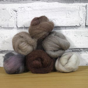 May include: Six balls of wool yarn in various shades of brown, grey, and beige. The yarn is arranged in a pyramid shape on a wooden surface.