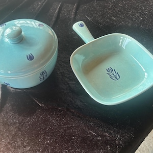 Op de afbeelding: Tweedelige turquoise keramische serveerset. De set bevat een kom met deksel en handvat en een vierkante schaal met handvat. Beide stukken hebben een donkerblauw bloemmotief. De kom heeft een diameter van ongeveer 15 cm.