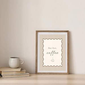 Könnte beinhalten: Ein gerahmter Druck mit dem Text "But first, coffee" in einer dekorativen Schriftart. Der Druck befindet sich in einem Holzrahmen und steht auf einer Holzoberfläche neben einem Stapel Bücher und einer Keramiktasse.
