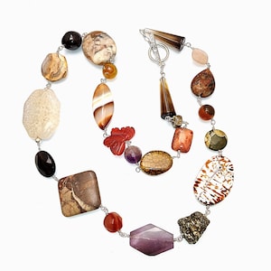 May include: A long necklace featuring a variety of multi-colored, multi-shaped natural stones and beads, including agate, amethyst, and jasper, connected by silver-toned metal links and finished with a toggle clasp closure.