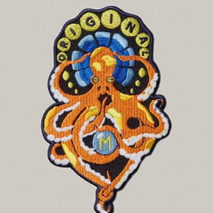 May include: Embroidered patch featuring an orange octopus with yellow and white accents. The octopus is surrounded by a blue and black design, with the word "ORIGINAL" in yellow letters. A blue circle with the letter "M" is in the center.