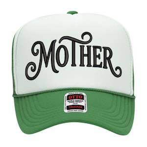 Könnte beinhalten: Grün-weiße Trucker-Cap mit dem Wort "MOTHER" in großen, schwarzen, stilisierten Buchstaben auf der Vorderseite. Die Kappe hat einen grünen Schirm und ein Mesh-Rückenteil mit einem kleinen Etikett auf der Vorderseite.