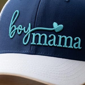 May include: Navy blue and white trucker hat with the words "boy mama" embroidered in teal script. The hat features a white brim and a white mesh back, perfect for casual wear.