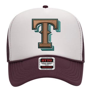Op de afbeelding: Een bordeauxrode en witte truckerpet met een grote, bruine letter "T" omlijnd met teal. De pet heeft een mesh achterkant en een druksluiting. Het label luidt "OTTO WORLD FAMOUS FOAM FRONT OSFM TRUCKER DURABLE SNAP CLOSURE".
