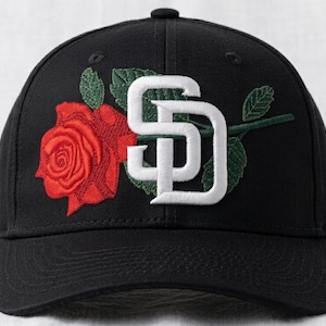 May include: Black baseball cap featuring a red rose and the letters "SD" in white. The rose is embroidered with green leaves and stem. The cap has a curved brim and a button on top.