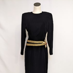 May include: A black velvet dress with long sleeves and a gold belt with a jeweled buckle.
