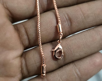 May include: A rose gold chain necklace with a snake chain design. The necklace has a lobster clasp closure. The chain is displayed against a neutral background.