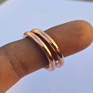 Op de afbeelding: Twee roségouden ringen, elk met een glad, afgerond ontwerp. De ringen zijn op elkaar gestapeld, waardoor een dubbele band ontstaat. De ringen worden op een vinger getoond, waarbij hun gepolijste afwerking en warme kleur worden benadrukt.