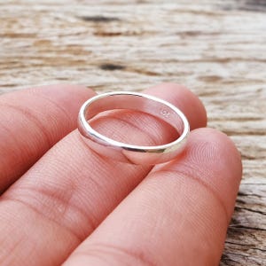 Puede incluir: Un anillo de banda de plata pulida con una superficie exterior lisa y redondeada. El interior de la banda de metal presenta un grabado claro del sello 925, lo que indica una composición de plata esterlina. El anillo tiene una forma sólida.