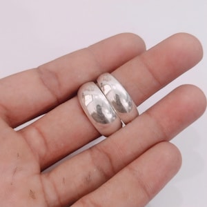 Peut inclure: Deux bagues argentées polies avec une surface lisse, arrondie et bombée. Les bagues présentent une finition métallique très brillante qui reflète la lumière, créant des reflets éclatants sur leur design en anneau plein et uni.