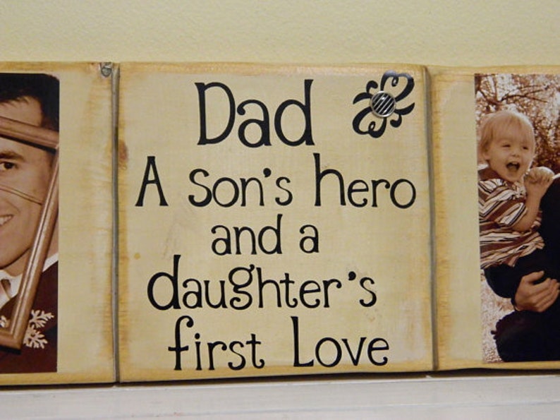 May include: A wooden sign with the text "Dad, A son's hero and a daughter's first love" in black lettering on a beige background. The sign is divided into three sections, with a photo of a man in the left section and a photo of a young boy in the right section.