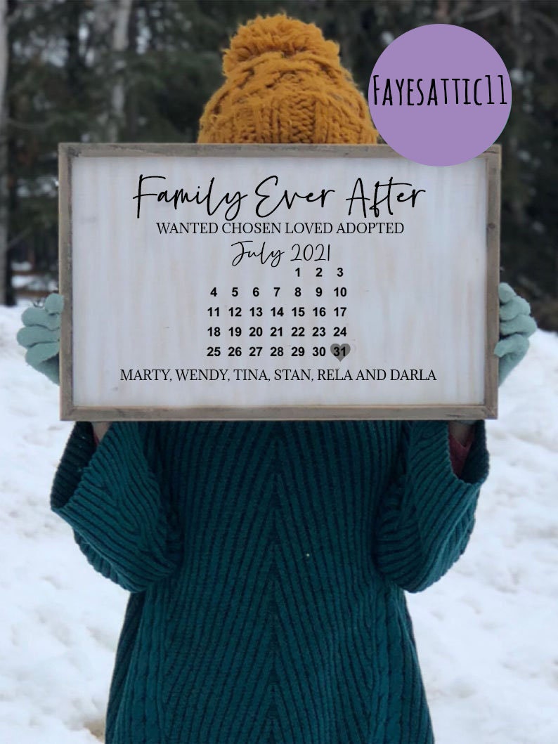 Puede incluir: Un letrero de madera blanco con el texto "Family Ever After" y "Wanted Chosen Loved Adopted" en letras negras. El letrero tambi&eacute;n incluye un calendario para julio de 2021 con los nombres "Marty, Wendy, Tina, Stan, Rela y Darla" en la parte inferior.