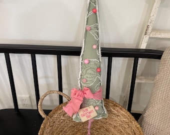 Puede incluir: Un árbol de Navidad decorativo de tela verde con estampado floral, adornado con adornos rosas y una estrella. Tiene un lazo rosa y una etiqueta que dice "Old Christmas Tree". El árbol está colocado en una cesta de mimbre.