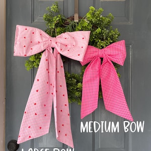 May include: Two decorative bows, one large and one medium, are displayed on a green wreath. The large bow is pink gingham with red hearts, and the medium bow is solid pink gingham. Text on the image reads "LARGE BOW" and "MEDIUM BOW".