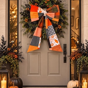 May include: A decorative wreath featuring dark green foliage and orange berries, adorned with a large, multi-patterned fabric bow. The bow displays a patchwork design of orange, black, white, and green plaid, gingham, and pumpkin-themed fabric prints.
