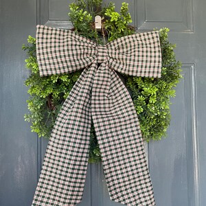 May include: A decorative wreath with a large plaid bow. The bow features a green, red, and white plaid pattern. The wreath is made of green foliage and is hanging on a blue door.