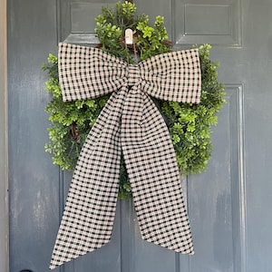 May include: A green wreath with a large plaid bow, hanging on a blue door. The bow features a pattern of black, white, and red squares. The wreath is made of small green leaves.