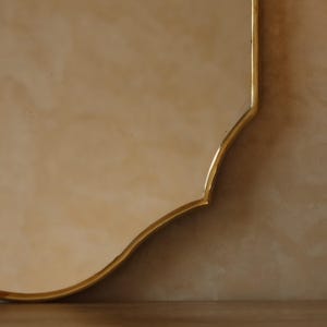 May include: A decorative mirror with a gold-colored, ornate frame. The mirror has a unique, curved shape and a warm, neutral background. The frame's design adds a touch of elegance to the overall aesthetic.
