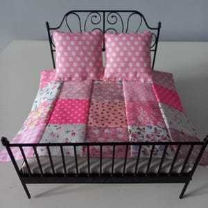 May include: Miniature black metal bed frame with a pink patchwork quilt and two pink polka dot pillows. The quilt features various pink floral and patterned fabrics, creating a charming, handcrafted aesthetic. A delightful piece for a dollhouse or decorative display.