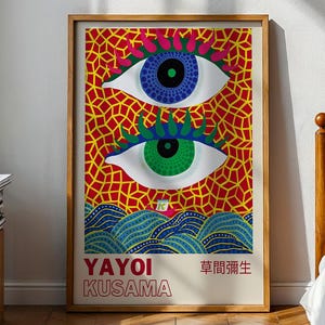May include: Framed art print featuring two stylized eyes with blue and green irises against a red and yellow background. The artwork includes the artist's name, "Yayoi Kusama," and Japanese text. The print is displayed in a room with a wooden floor and a bed.
