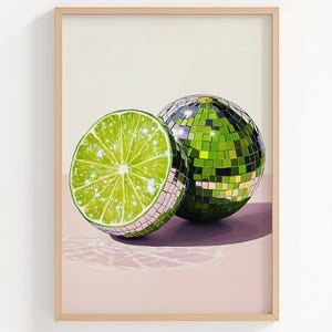 May include: A framed art print featuring a lime slice and a disco ball. The lime slice is bright green with a sparkling effect, while the disco ball is covered in reflective green squares. The background is a soft pink and white.