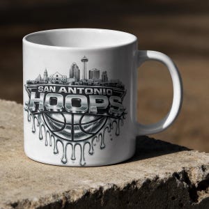 May include: White ceramic mug featuring the text "SAN ANTONIO HOOPS" in a silver, dripping font, with a basketball design. The mug also displays a skyline of San Antonio, Texas.
