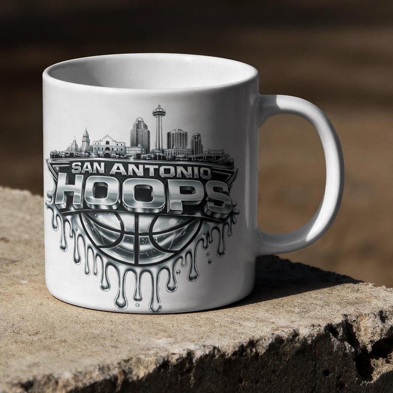 May include: White ceramic mug featuring the text "SAN ANTONIO HOOPS" in a silver, dripping font, with a basketball design. The mug also displays a skyline of San Antonio, Texas.