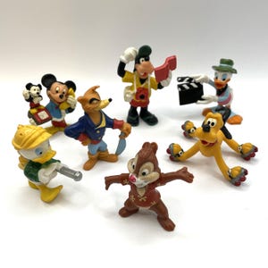 May include: A collection of Disney character figurines, including Mickey Mouse, Donald Duck, Goofy, Pluto, and Chip and Dale. The figurines are brightly colored and depict the characters in various poses, some holding props.