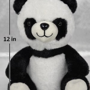 May include: A plush panda bear, approximately 12 inches tall, with a black and white color scheme. The panda has black ears, eye patches, arms, and legs, with a white body and face. It has a black nose and a smiling expression.