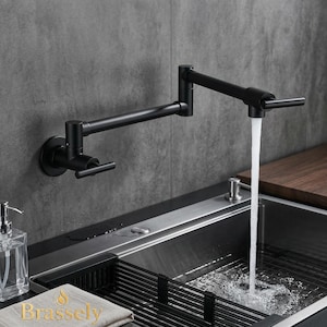 Puede incluir: Un grifo de cocina negro mate montado en la pared con un diseño de brazo oscilante. El grifo está colocado sobre un fregadero de acero inoxidable, con agua que fluye del caño. También se ven un dispensador de jabón y un escurreplatos.