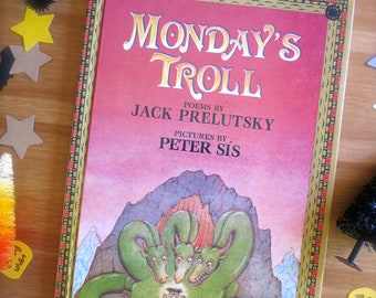 以下が含まれることがあります： ジャック・プレルツキー著、ピーター・シス画の絵本「Monday's Troll」。表紙には緑色の三つ頭のドラゴンが描かれています。ハロウィーンをテーマにした装飾が施されています。