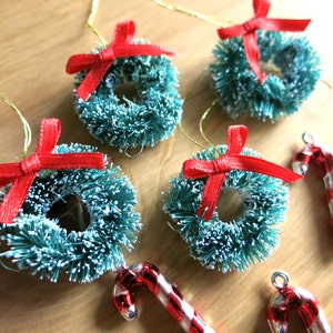 May include: Four miniature Christmas wreaths with red bows and a snowy green finish, and two candy cane ornaments.
